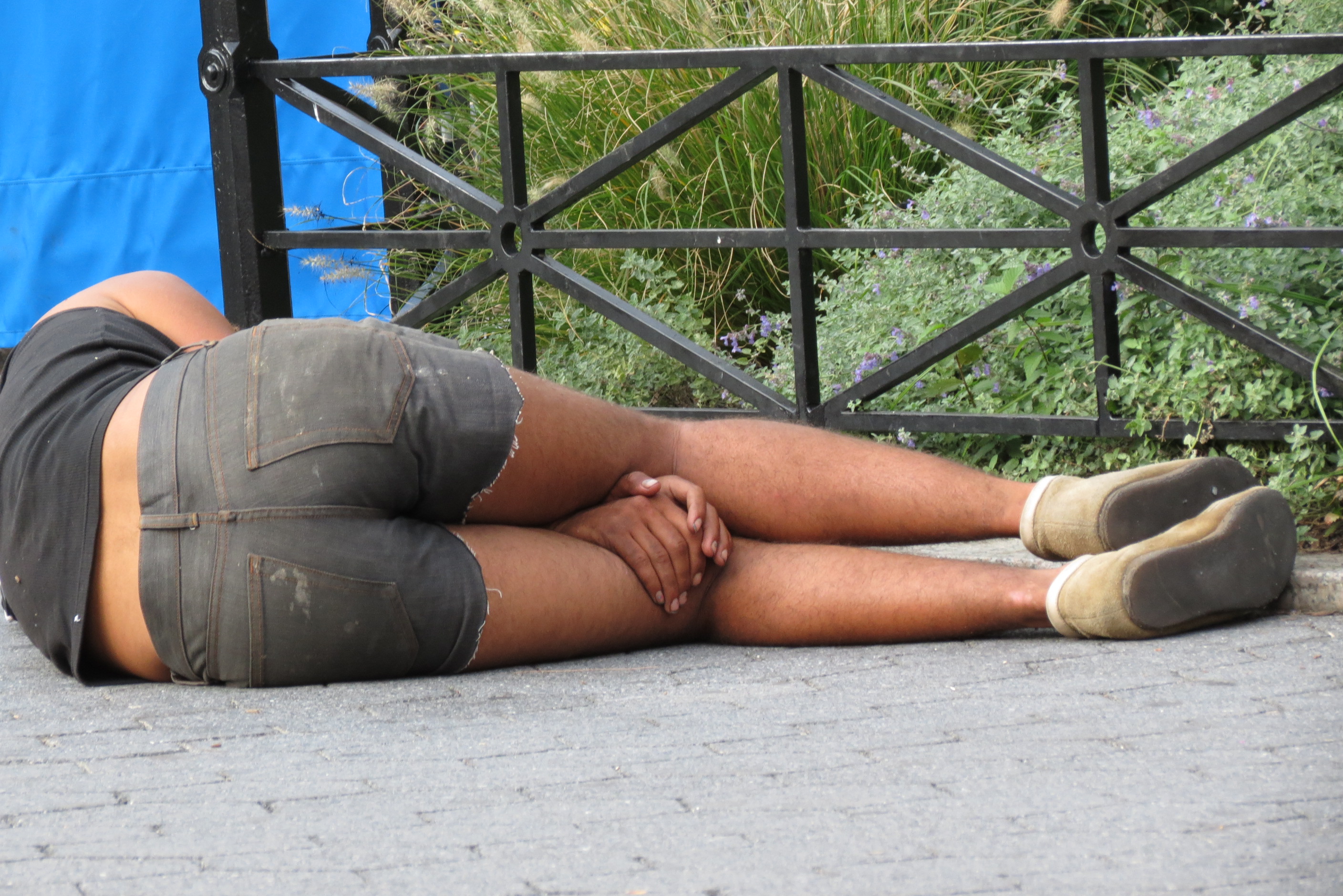 Homeless man in shorts sleeping with hands between knees