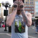 man with eyes tattooed on hands covering face