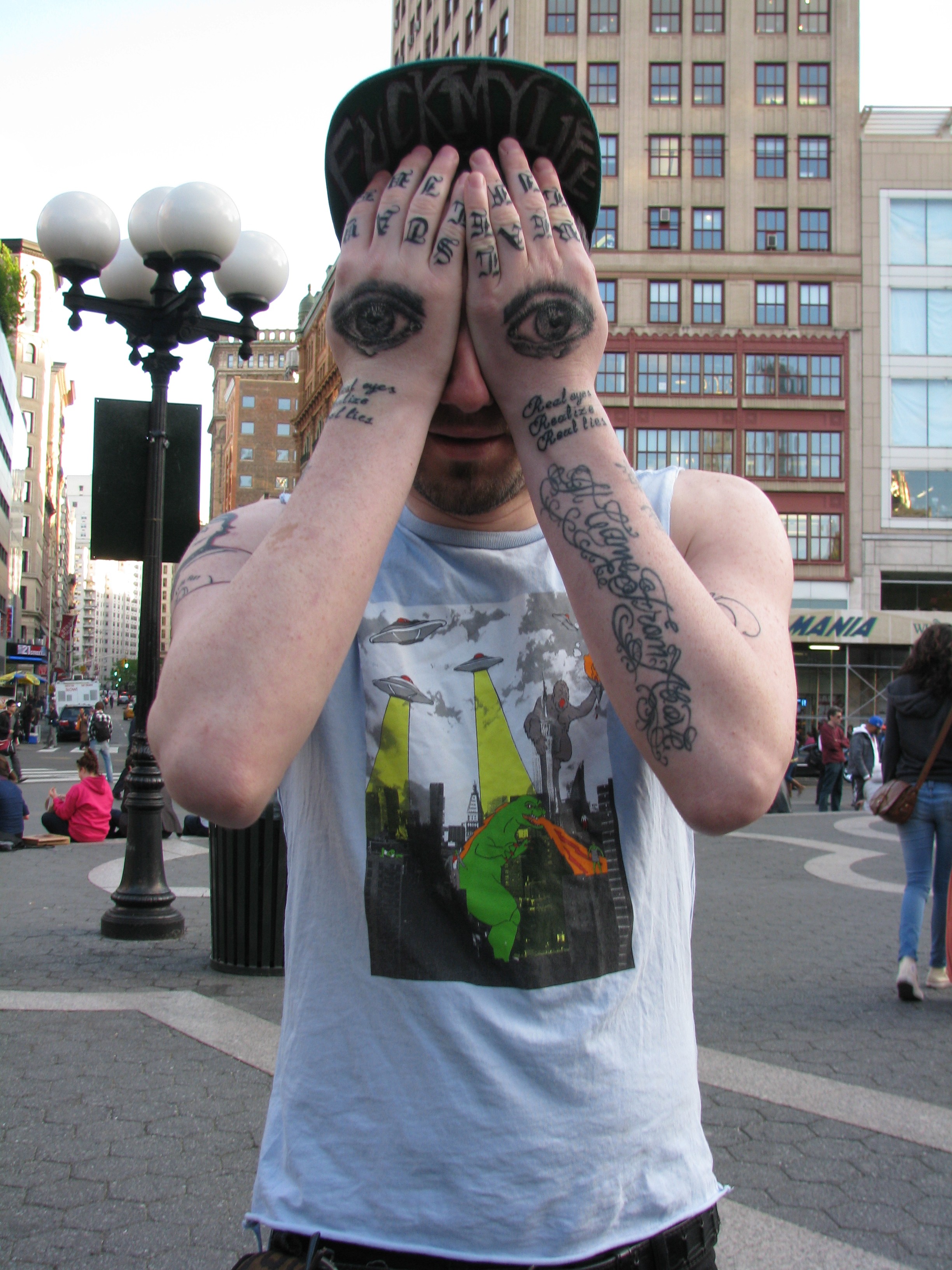 man with eyes tattooed on hands covering face