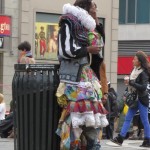 homeless fashion designer stands against garbage can